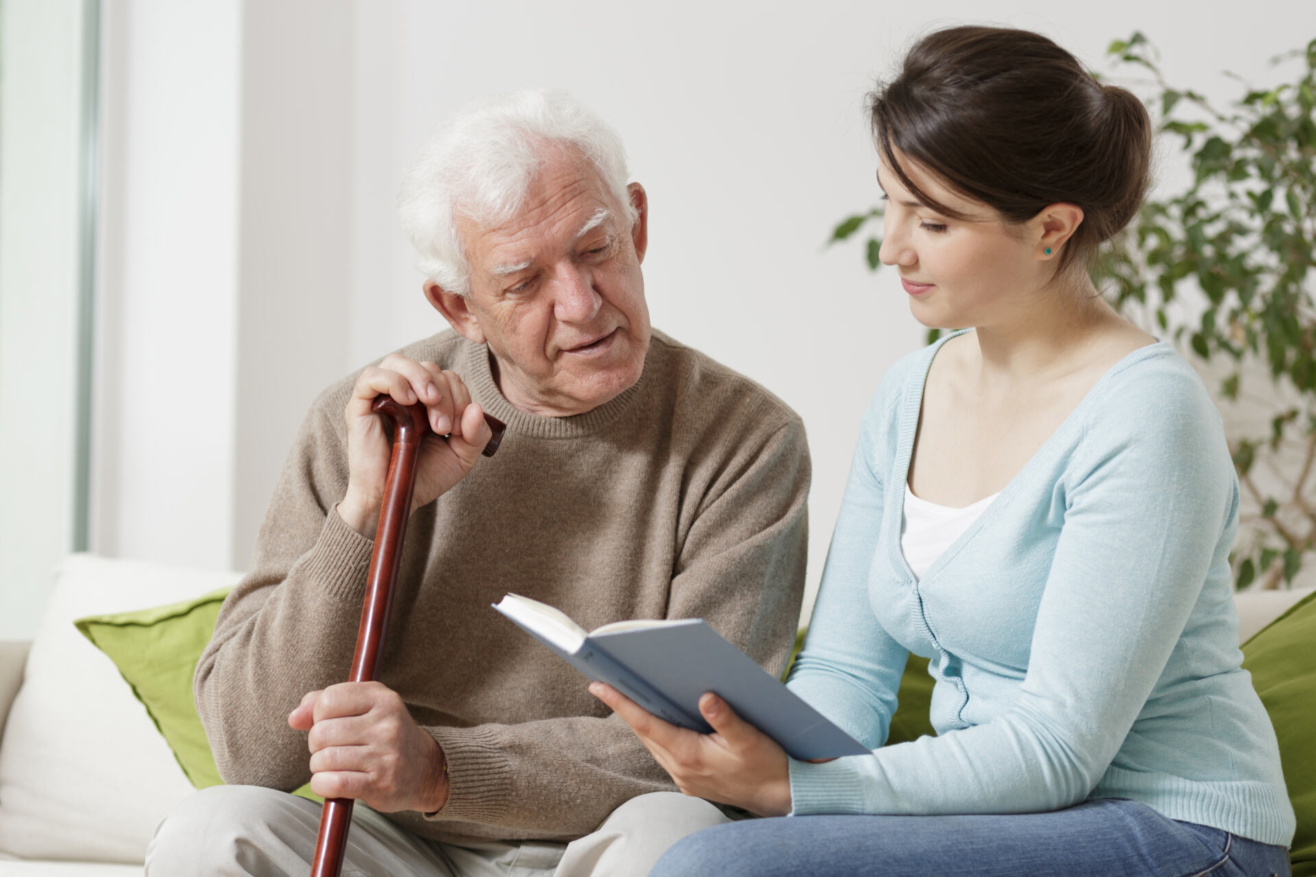 Image of young carer reading book to senior man