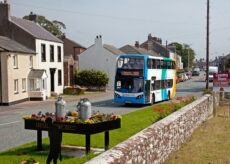 A Stagecoach bus driving through a town with grass and flowers in the foreground