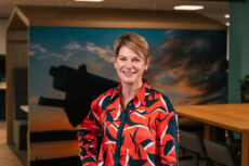 An image showing a woman with short dark blonde hair wearing a colourful red and navy blue blouse.