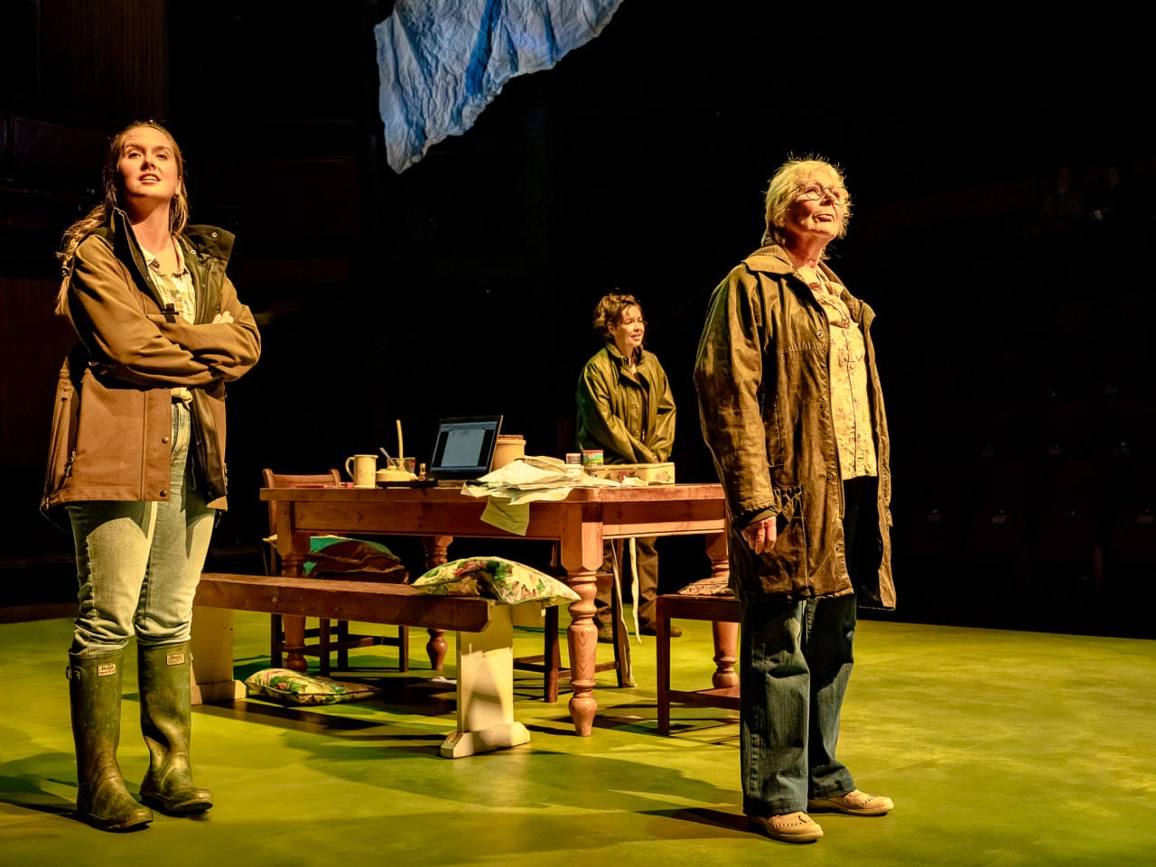 Three women staring on stage around a kitchen table.